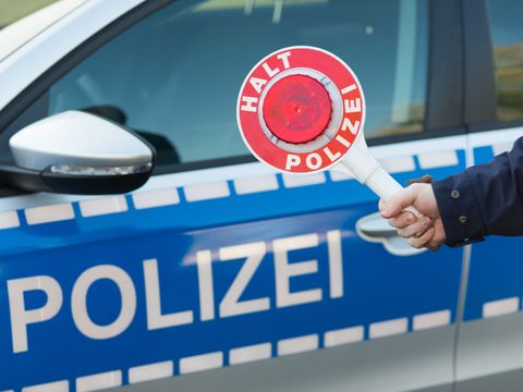 Tür eines Polizeiautos mit davorgehaltener Polizeikelle