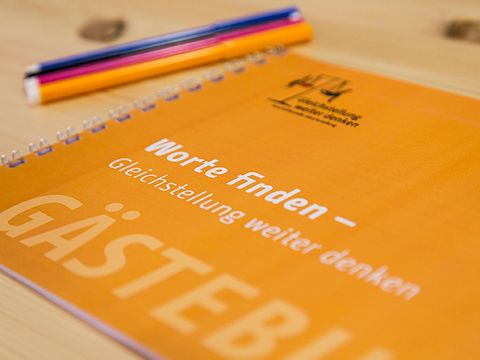 Auf dem Holzblatt liegt das Gästebuch, neben zwei Stifte