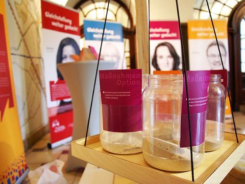 Gefüllte Behälter der Waage sind im Vordergrund zu sehen, im Hintergrund vier Promi-Plakate