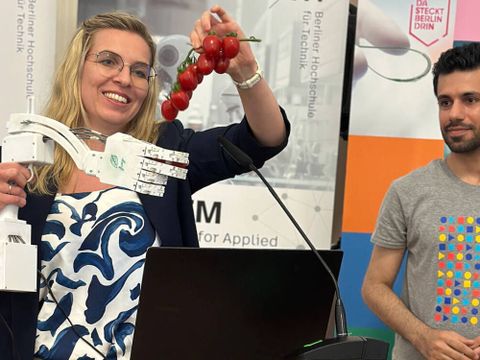 Eine Frau präsentiert eine Roboterhand die nach Tomaten greift