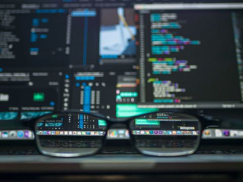 Eine Brille liegt vor einem Monitor mit Computercode