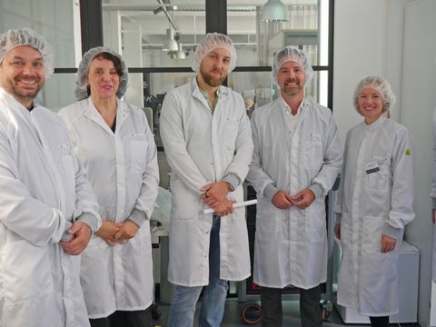 Eine Gruppe von Wissenschaftlern in weißen Kitteln und Haarhauben
