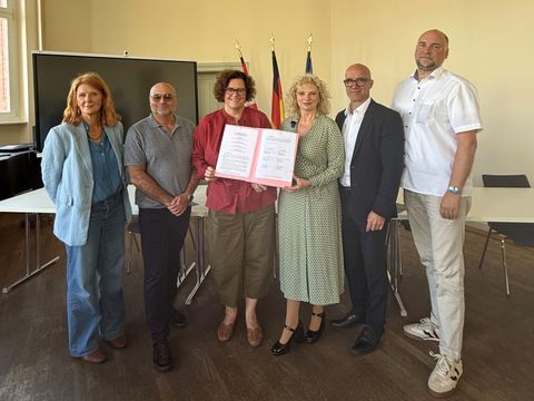 Sechs Personen stehen zusammen. Die Personen in der Mitte halten eine geöffnete Dokumentmappe in der Hand.