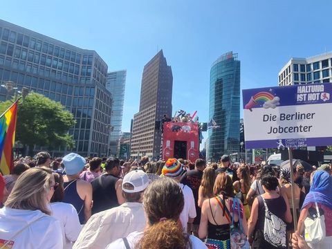 Viele Menschen auf einer Parade mit Accessoires in Regenbogenfarben und einem Schild mit dem Text: Haltung ist Hot. Die Berliner Jobcenter.