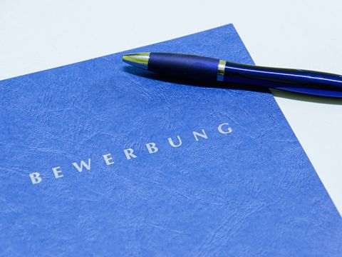 Auf einem Blatt steht Bewerbung , daneben liegt ein Kugelschreiber