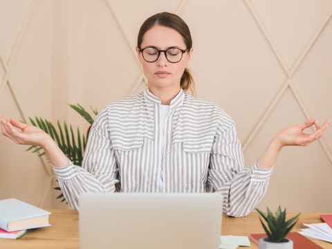 Businesswoman meditating yoga practice on workplace after hard day, deadline concept. Stress relief