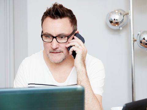 Mann sitzt telefonierend vor einem Laptop.