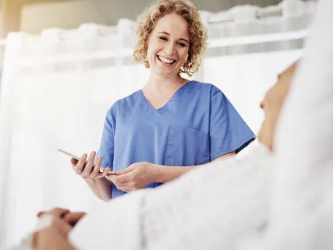 Eine lächelnde Krankenpflegerin spricht mit einem liegenen Patienten