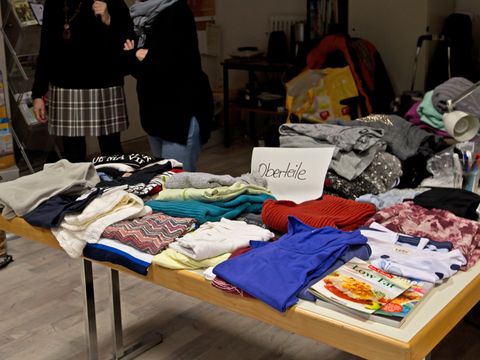 Kleidung auf einem Tisch für einen Kleidertausch. Menschen im Hintergrund unterhalten sich.