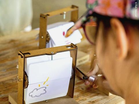 Person bedient kleinen Holzapparat mit auf Papier gezeichneter Wolke darin