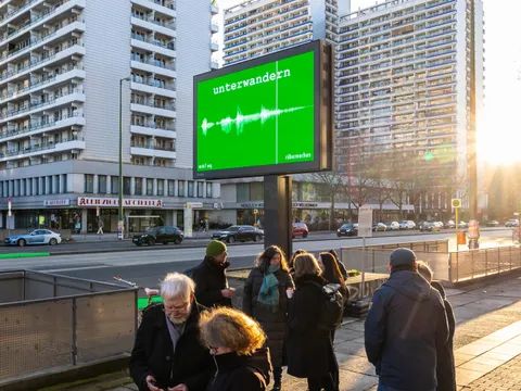 Straße in der Abendsonne mit grüner Werbetafel, darauf steht "unterwandern"