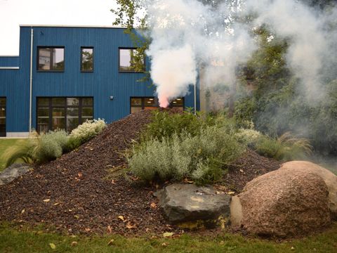 Vulkan aus Lavagestein mit Rauch und blaues Haus im Hintergrund