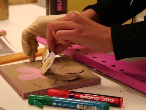 Nahaufnahme einer Hand, die eine gold übermalte Blumen-Schablone von einer rosa bemalten Holzplatte zieht