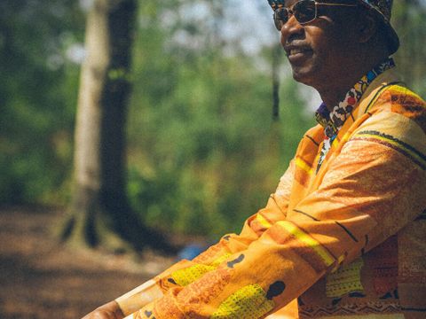 Ein farbiger Mann, der lächelt im Wald mit Sonnenbrille gelben Sakko und roter Hose