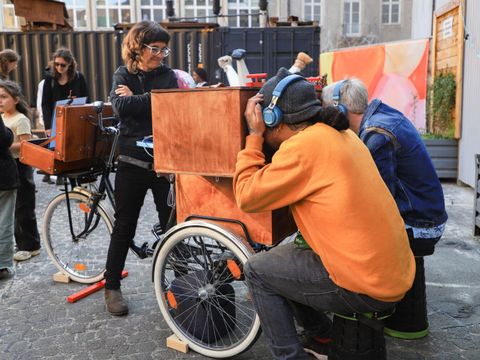 Menschen an einem großen Fahrrad, die in eimem Holzkasten schauen.