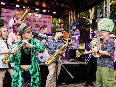 Eine Band von Brass-Musiker*innen vor und auf der Bühne mit bunten Kostümen