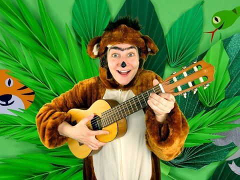 Ein junger lachender Mensch in einem Affenkostüm mit Gitarre