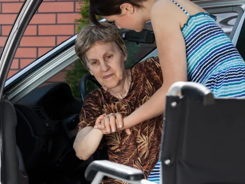 Frau hilft älterer Frau aus dem Auto