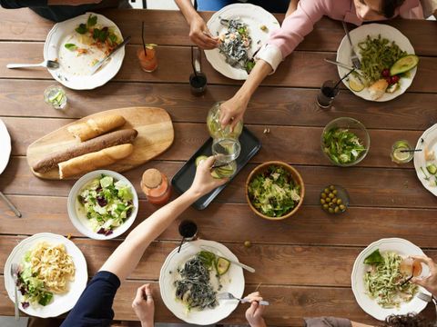 Tisch mit 8 Tellern von oben fotographiert. Zwei Gläser die anstoßen. Brot und Salate in der Mitte