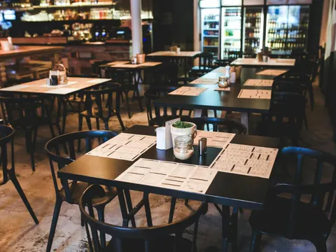 Restaurant mit schwarzen Tischen und Speisekarten. Im Hintergrund Theke und Flaschen im Kühlschrank