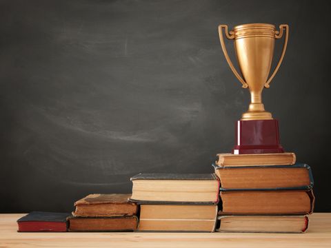 Ein Stapel von Büchern, angeordnet wie eine Pyramide mit einer goldenen Trophäe obenauf.