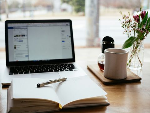 Ein Tisch auf dem ein aufgeschlagenes Buch vor einem offenen Notebook liegt