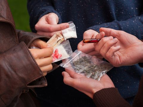 Mehrere Hände halten unterschiedliche Drogen und Geld in der Hand