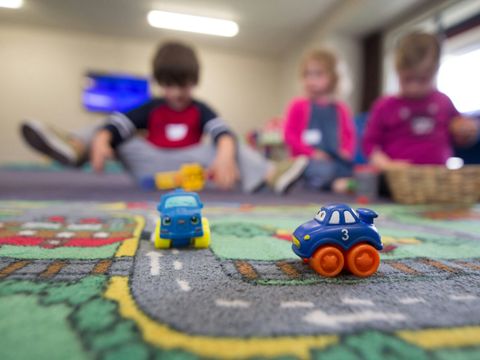 Kinder spielen mit Autos auf einem Spielteppich.