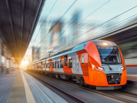 Electric passenger train drives at high speed among urban landscape.