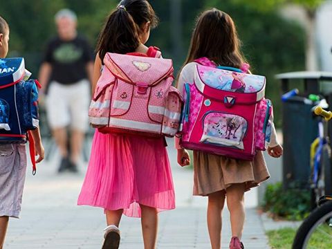 Ein Junge und zwei Mädchen aus der Grundschule mit Schul-Taschen