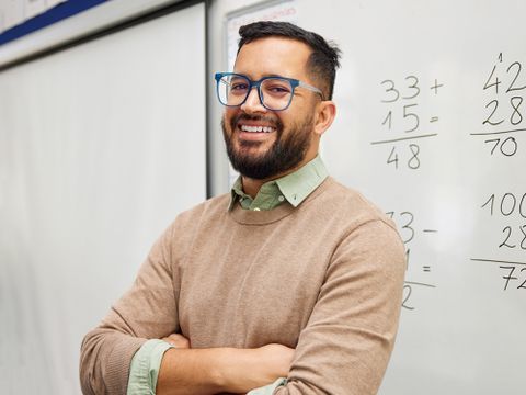 Lehrkraft - fröhlicher Mathelehrer vor Whiteboard mit Rechnungen