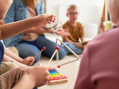 Musiktherapie - Gruppe mit Kindern und Erwachsenen sitzen auf dem Boden mit Musikinstrumenten wie Triangel