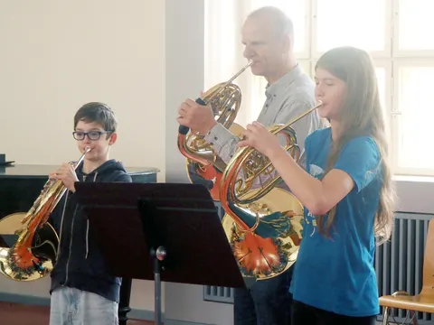 Zwei Schüler mit Lehrer blasen ins Horn