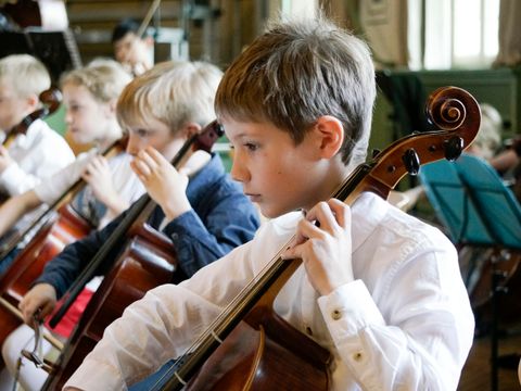 Jungs spielen konzentriert Cello.