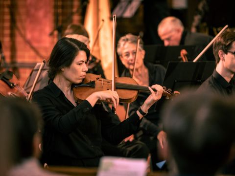 Mehrere Menschen spielen Streichinstruemnte im Orchester