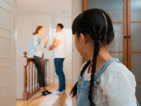 Kind im Vordergrund, guckt zu Eltern, die sich im Hintergrund streiten
