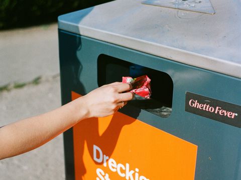 Die Hand einer Person wirft Müll in einen Mülleimer auf der Straße.