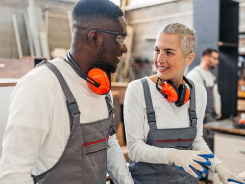 Mann und Frau unterhalten sich in einer Werkstatt, mehrere Menschen sind im Hintergrund