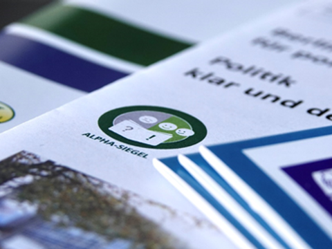 Mehrere Broschüren mit Logos "Leicht Lesen", "ALPHA-SIEGEL" und "Leichte Sprache"