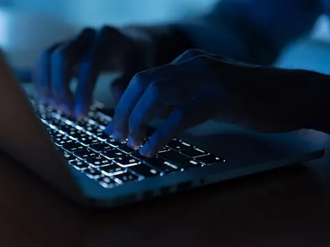 Hände auf einer beleuchteten Laptoptastatur im abgedunkelten Raum