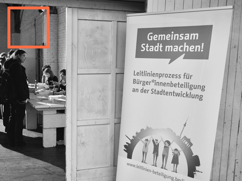 Roll-Up der Werkstatt zur Leitlinienerarbeitung, Personen im Hintergrund, Rahmen in orange