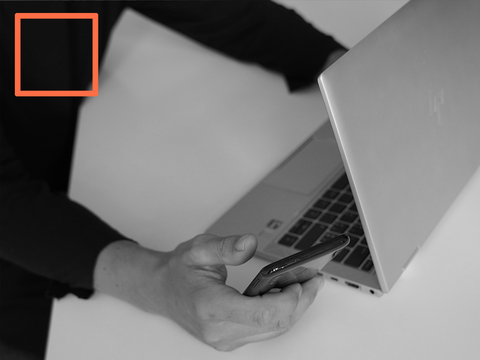 Person mit Handy an einem Laptop, quadratischer Rahmen
