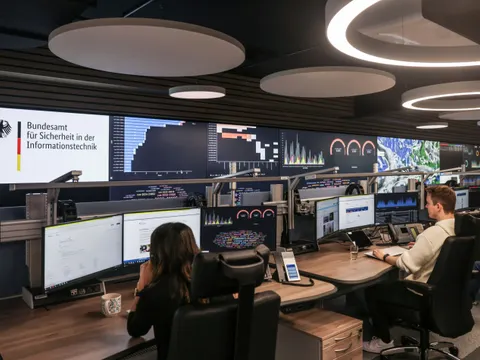 Büro des Bundesamt für Sicherheit in der Informationstechnik. Zwei Mitarbeitende sitzen an ihren Arbeitsplätzen vor mehreren Bildschirmen.
