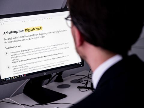 Ein Mann sitzt an einem Schreibtisch und schaut auf einen Computer-Monitor. Auf dem Bildschirm ist eine Anleitung zum Digitalcheck zu sehen.
