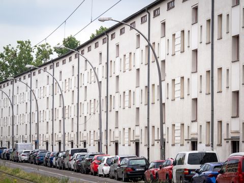 Mehrere Wohnhäuser stehen lückelnlos nebeneinander entlang einer Straße. DIe Häuser haben eine weiße Fassade.