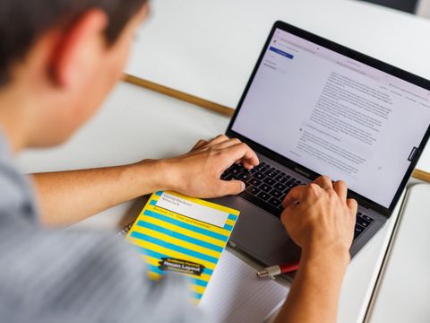 Ein Schüler tippt auf einem Laptop. Vor ihm liegt das Buch "Woyzeck" von Georg Büchner.