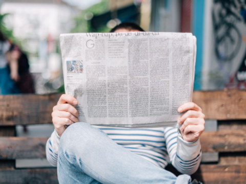 Ein Mann sitzt auf einer Bank und liest eine Zeitung.