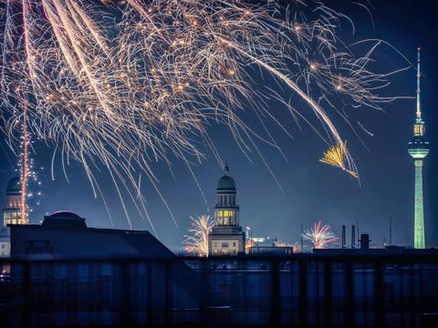 Abendliches Silvester-Feuerwerk mit Silhouette der Stadt Berlin.