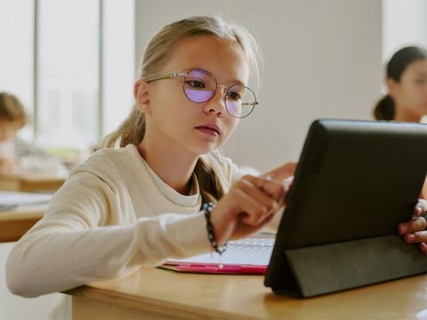 Schülerin sitzt im Klassenraum und arbeitet an einem Tablet
