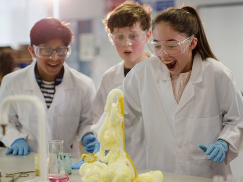 Gruppe von Schülern expertimentiert im Chemieunterricht und freut sich über eine chemische Reaktion